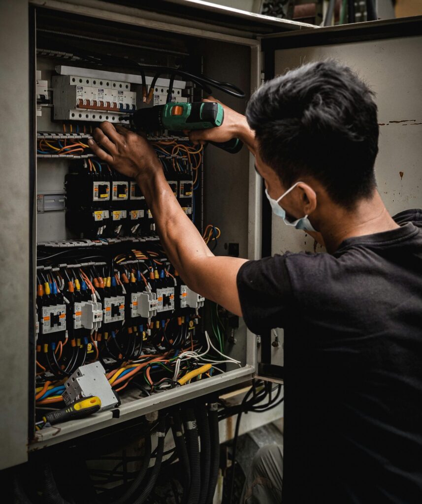 Technician working on circuit breaker panel, adjusting electrical wires indoors.
